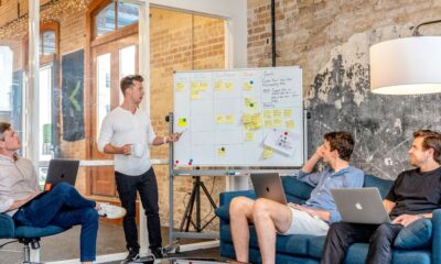 three men sitting while using laptops and watching man beside whiteboard